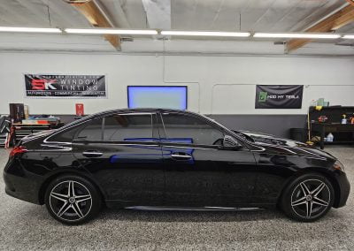 A black sedan inside a garage in Irvine, with banners for window tinting and Tesla services on the wall behind it.