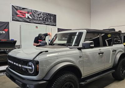 A gray SUV is parked in a garage featuring a worker in the background and a banner that reads "SK Window Tinting," showcasing their expert car window tint services.
