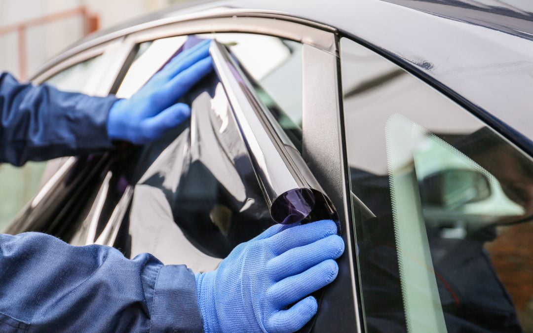 A person wearing blue gloves is expertly applying window tint to a car window in sunny California.